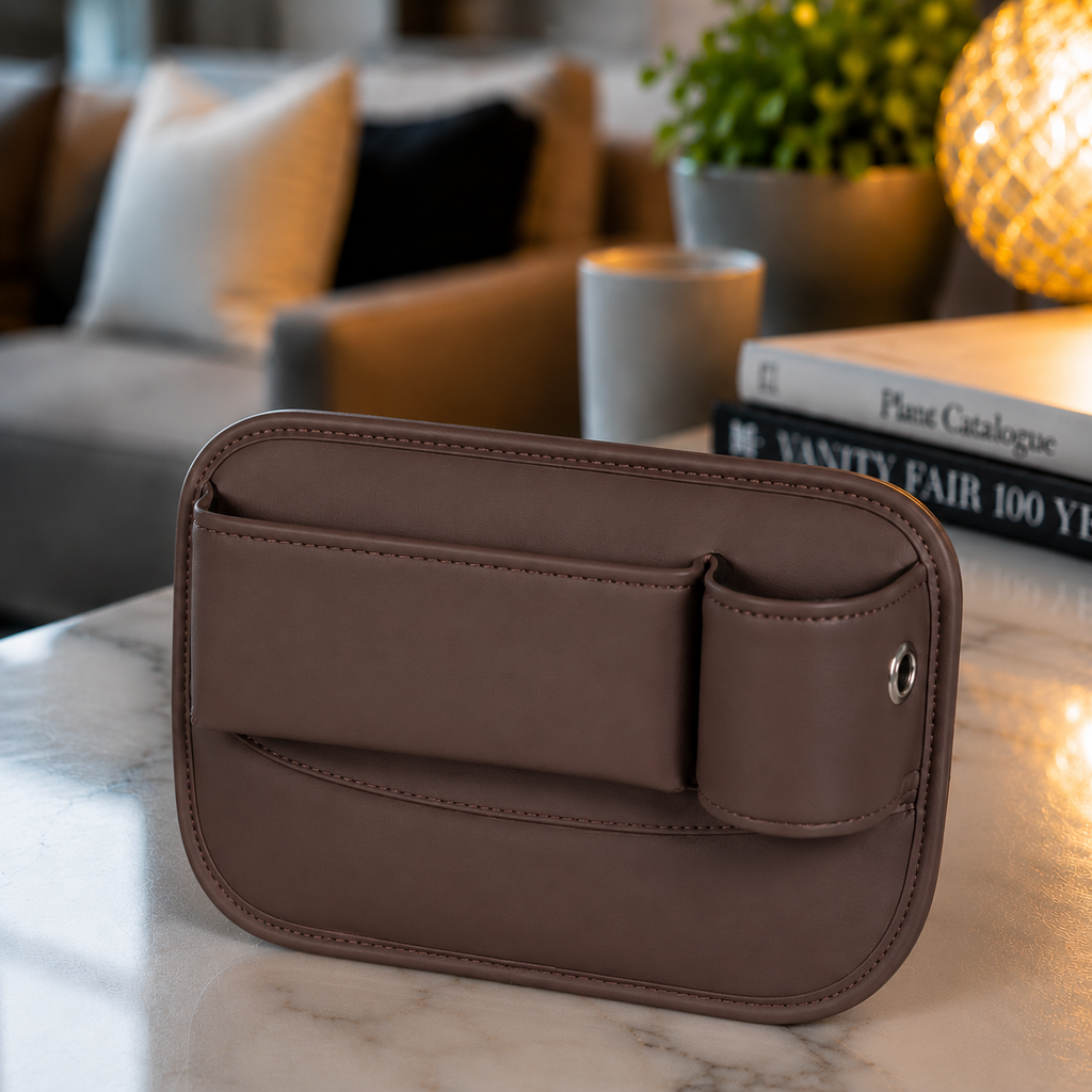 A brown faux-leather phone pouch with a front slip pocket and snap button closure, resting on a white marble tabletop in a modern living room setting.